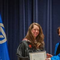 Provost Mili presents certificate to woman on stage